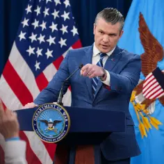Minister obrony w garniturze przemawia przy mównicy z godłem USA. Za nim amerykańska flaga i sztandar z orłem.