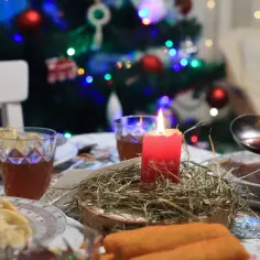 Wigilia w blasku świecy. Na stole pierogi, barszcz i napoje. W tle choinka. Wolna wigilia w gronie najbliższych.