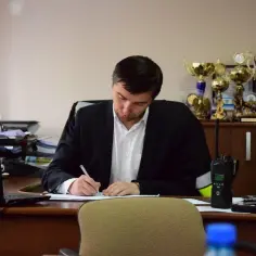 Mężczyzna w garniturze pisze przy biurku, na którym leży laptop i krótkofalówka. Za nim na półce stoją puchary. Zastanawia się, ile trwa kadencja wójta.