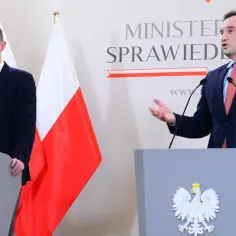 Dwóch mężczyzn w garniturach przemawia za mównicami z godłem Polski. Jeden z nich ma maseczkę. Dyskutują o tym, impeachment co to znaczy w polskim prawie.