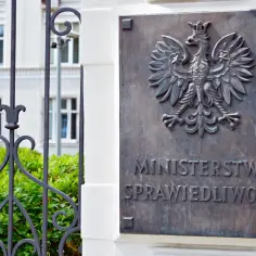 Tablica z godłem Polski i napisem "MINISTERSTWO SPRAWIEDLIWOŚCI". Za nią widać fragment budynku i zieleni.