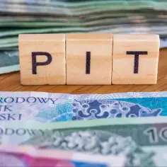 Drewniane klocki z literami "PIT" na tle polskich banknotów. Nadzieja na ulga na dzieci 2026.
