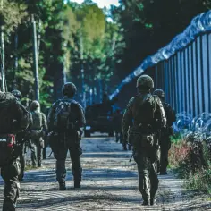 Żołnierze patrolują granicę polsko-białoruską. W tle widać druty kolczaste i las.