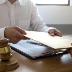 Przekazanie koperty z dokumentami, być może w sprawie o subwencję, obok młotka sędziowskiego.