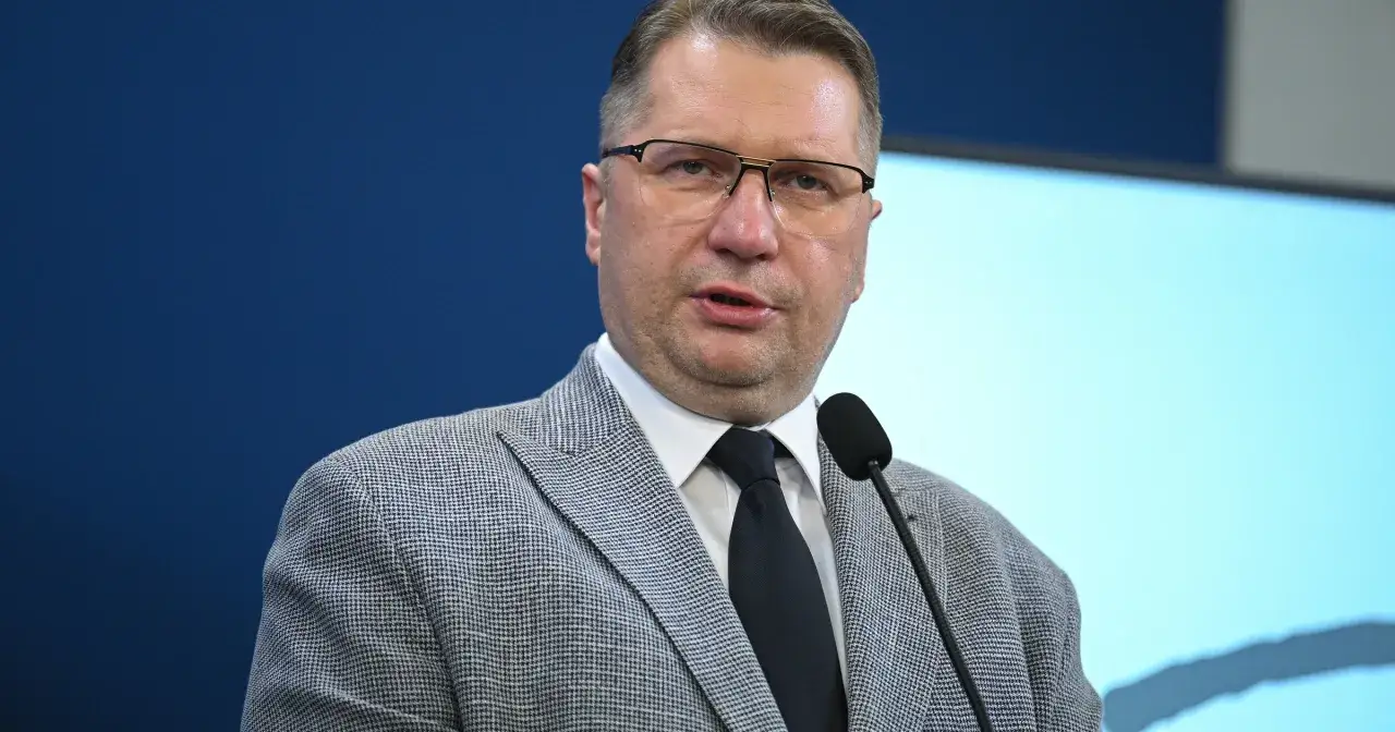 Premier polski w okularach, w garniturze i krawacie, przemawia przy mikrofonie.