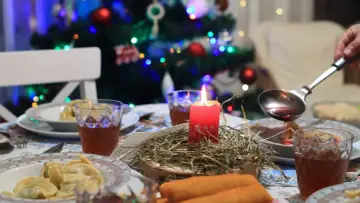 Wigilia w blasku świecy. Na stole pierogi, barszcz i napoje. W tle choinka. Wolna wigilia w gronie najbliższych.