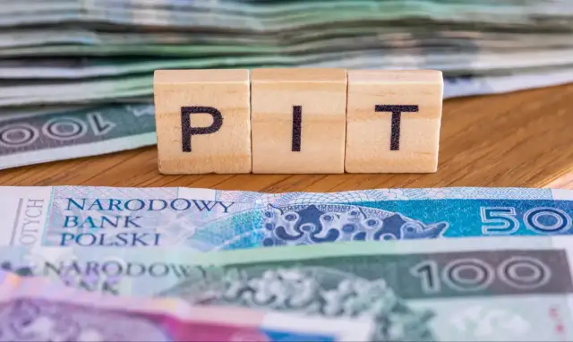 Drewniane klocki z literami "PIT" na tle polskich banknotów. Nadzieja na ulga na dzieci 2026.